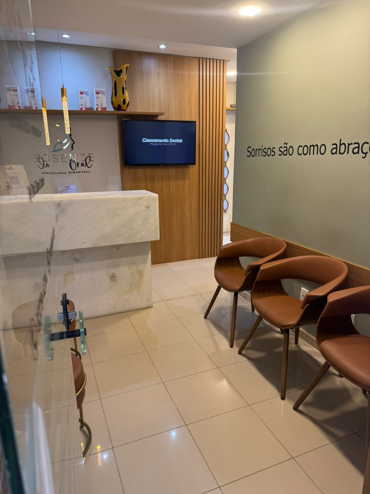 Recepção da Essence Oral com balcão de mármore, painel de madeira e poltronas de espera