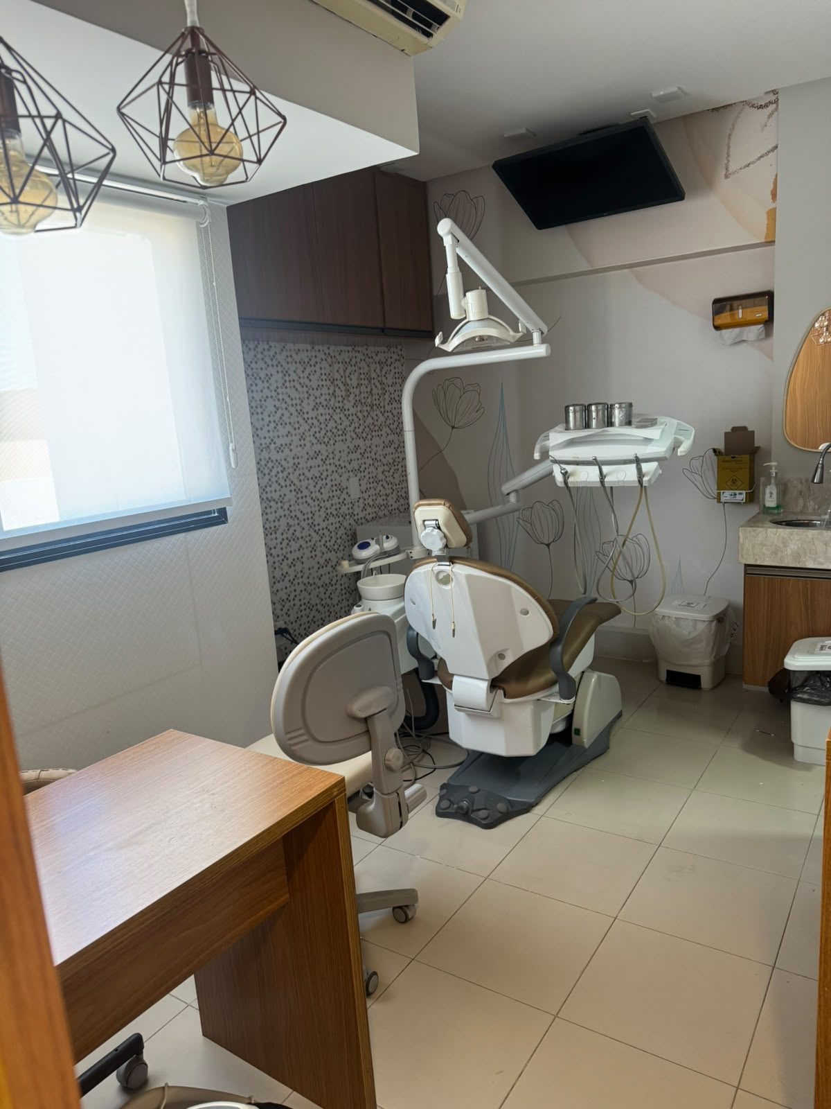 Sala de atendimento da Essence Oral com cadeira odontológica, luminárias pendentes e decoração floral